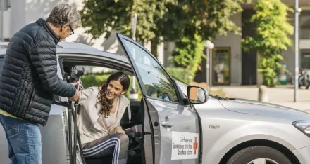 Ein freiwilliger Fahrer des SRK Fahrdienst hilft einer jungen Frau beim Aussteigen aus dem Auto.