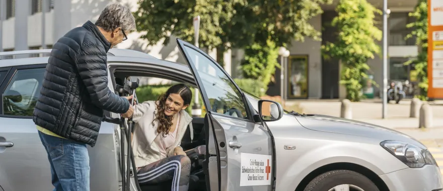 Ein freiwilliger Fahrer des SRK Fahrdienst hilft einer jungen Frau beim Aussteigen aus dem Auto.